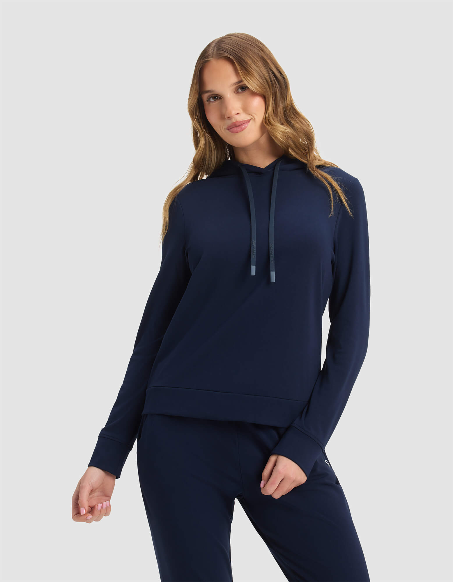 A woman with long, wavy light brown hair smiles gently, wearing the Cozy Earth Women's Brushed Bamboo Hoodie in navy against a plain light gray background.