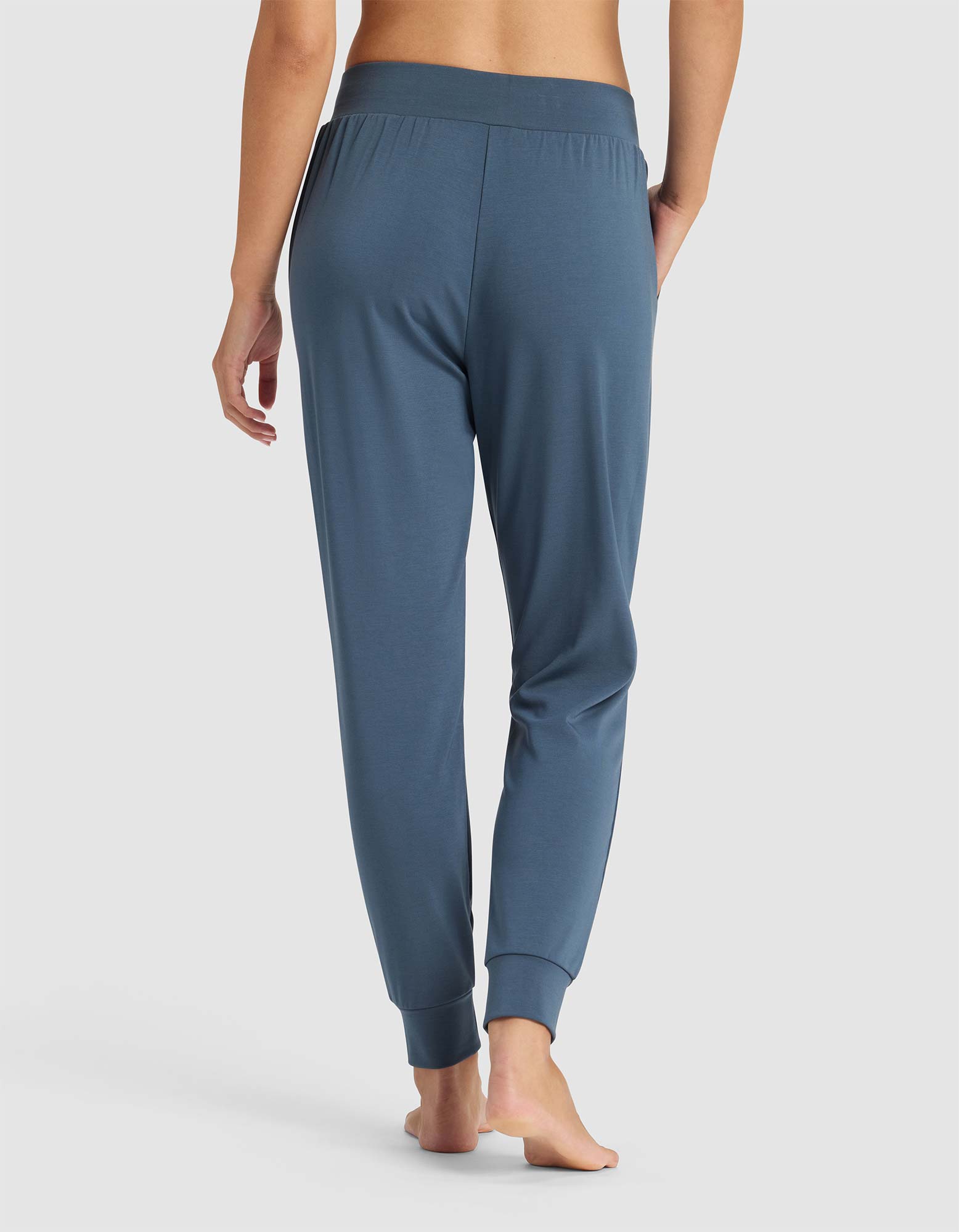 A woman stands barefoot, facing away, wearing Cozy Earth's Women's Brushed Bamboo Jogger Pant with an elastic waistband and cuffed ankles, shown against a plain white background.