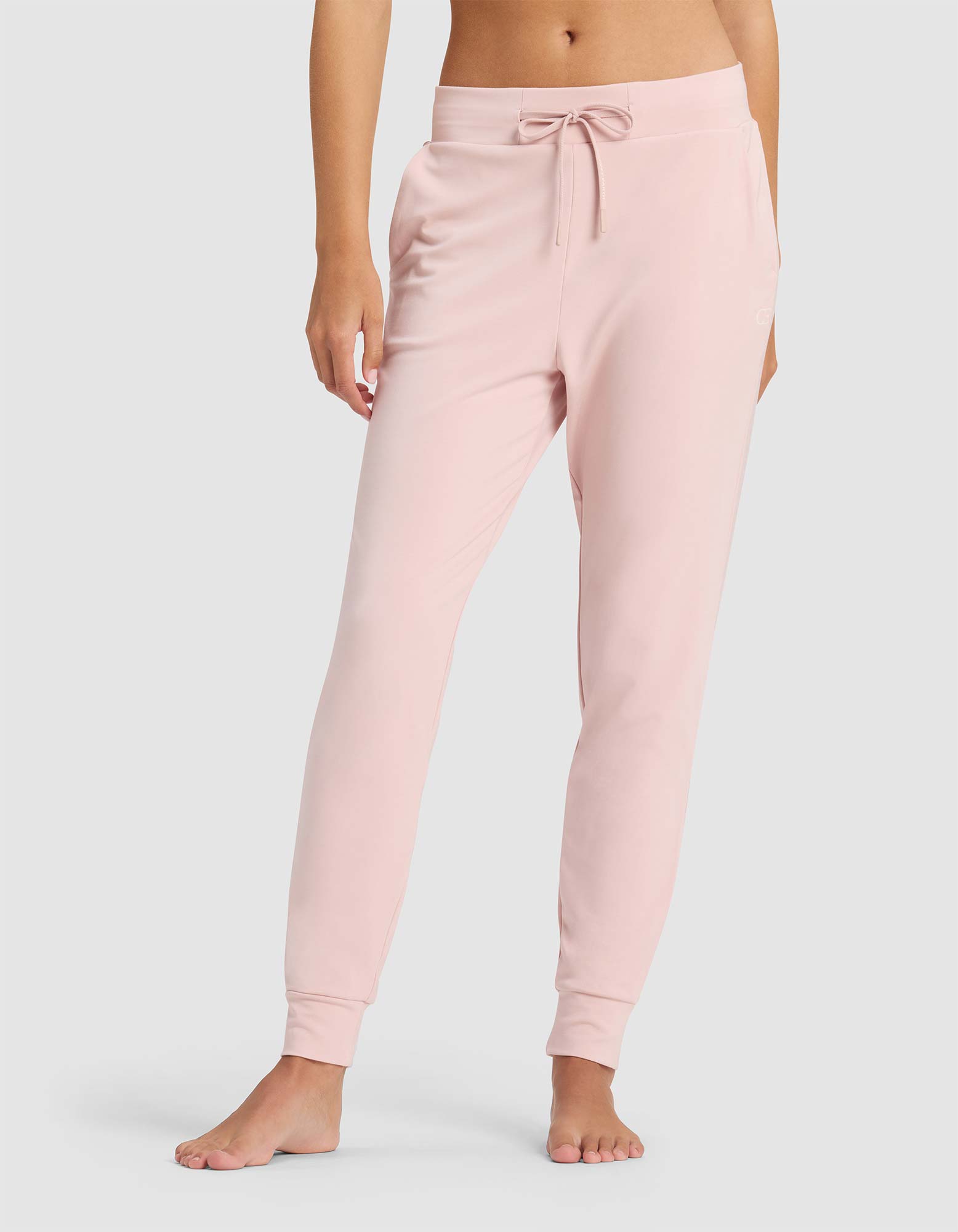 A woman stands barefoot against a plain light background, showing only the lower half of her body in Cozy Earth's Women's Brushed Bamboo Jogger Pant—light pink, with a drawstring waist.