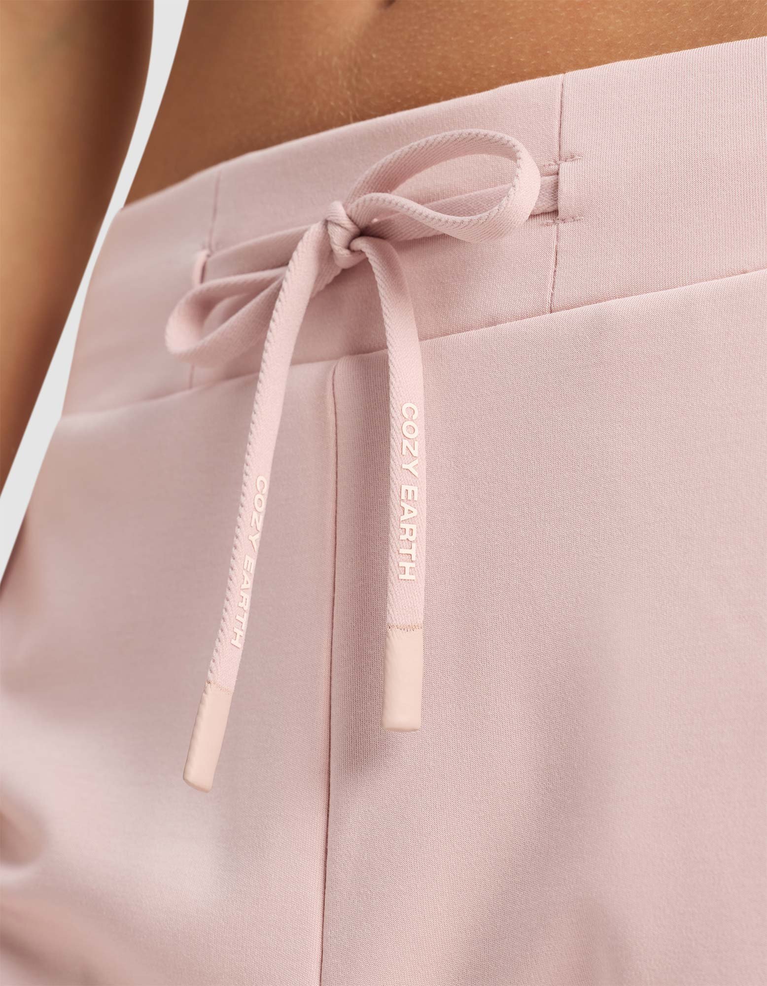 Close-up of Women's Brushed Bamboo Jogger Pant by Cozy Earth in pale pink, featuring a soft, comfortable fabric and a drawstring waistband tied in a bow with "COZY EARTH" printed in white.