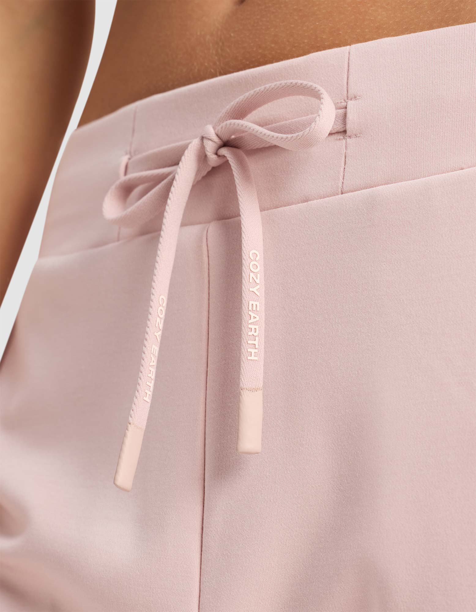 Close-up of Women's Brushed Bamboo Jogger Pant by Cozy Earth in pale pink, featuring a soft, comfortable fabric and a drawstring waistband tied in a bow with "COZY EARTH" printed in white.