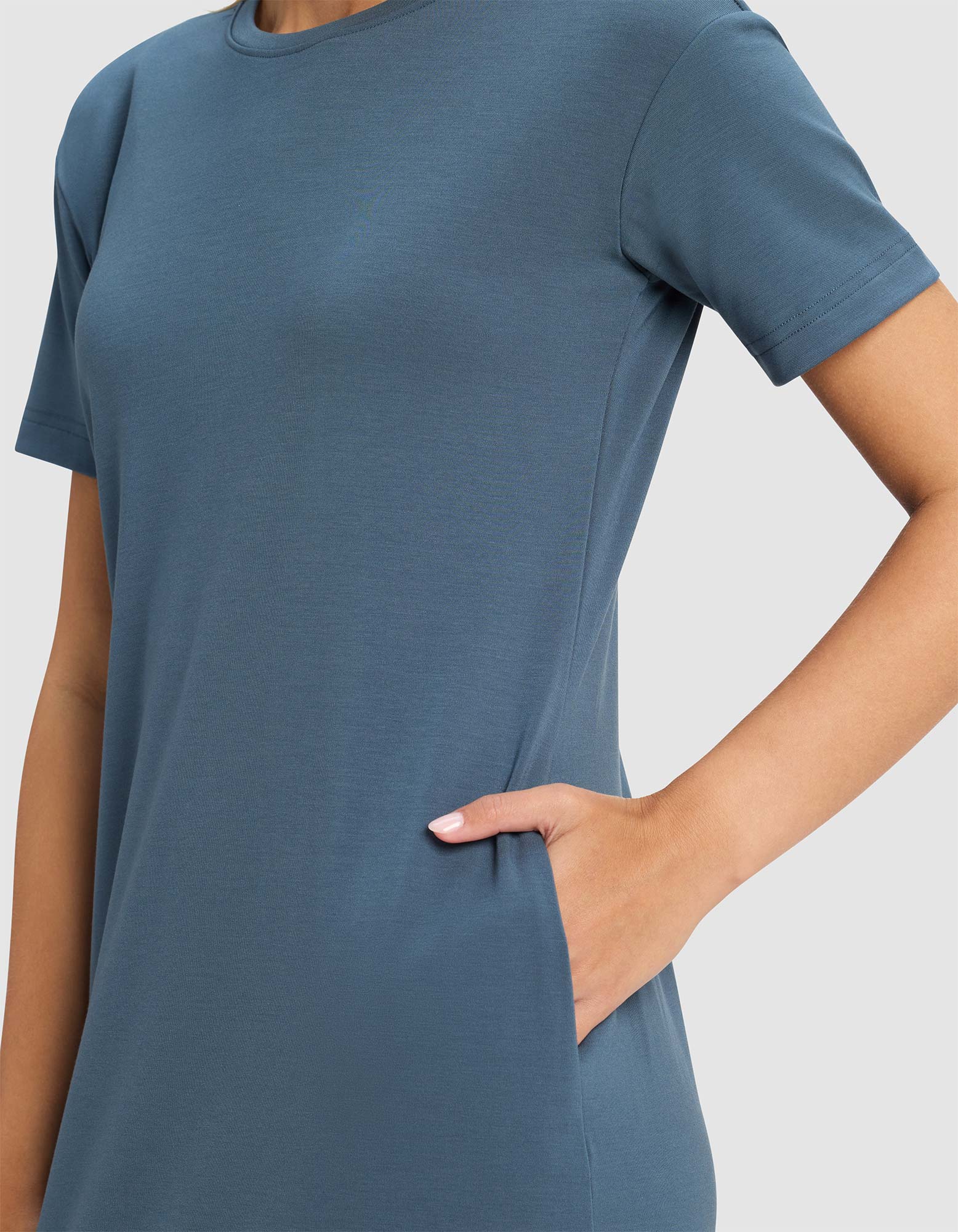 A person wears the Cozy Earth Women's Brushed Bamboo Midi Dress, a short-sleeve blue style with side pockets, standing against a plain light background.