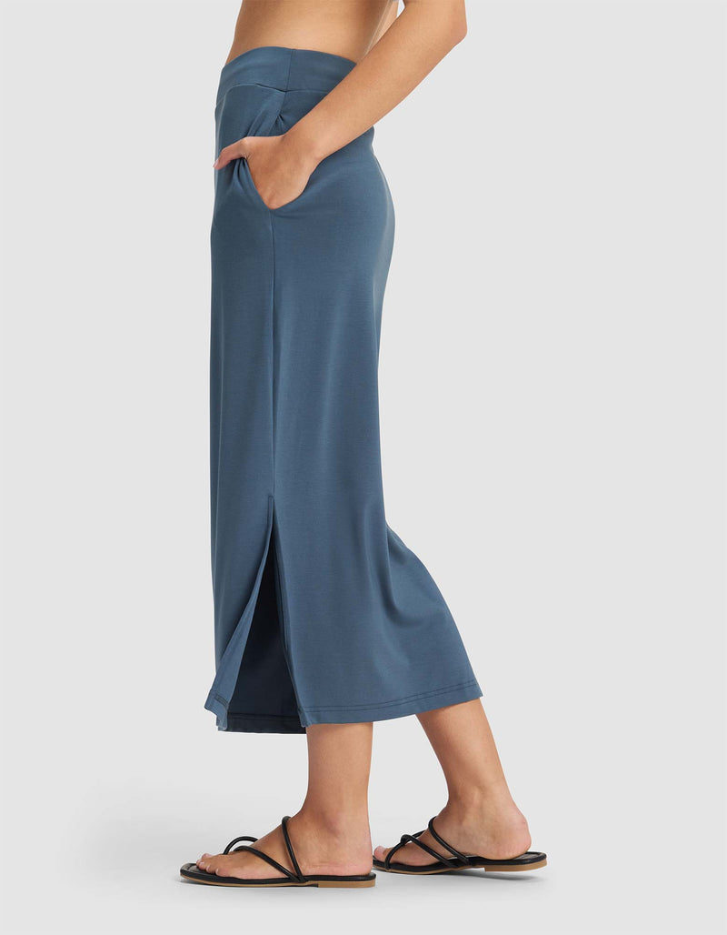 A woman wears the Cozy Earth Women's Brushed Bamboo Midi Skirt, standing sideways with one hand in her pocket against a plain light background.