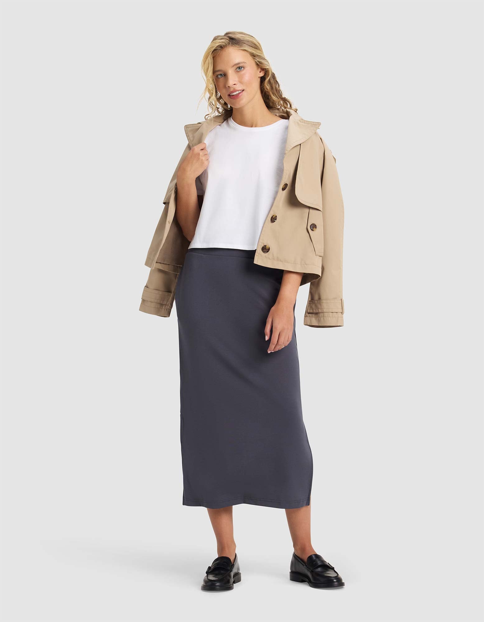 Woman wearing a beige jacket, white shirt, and gray skirt on a white background 
