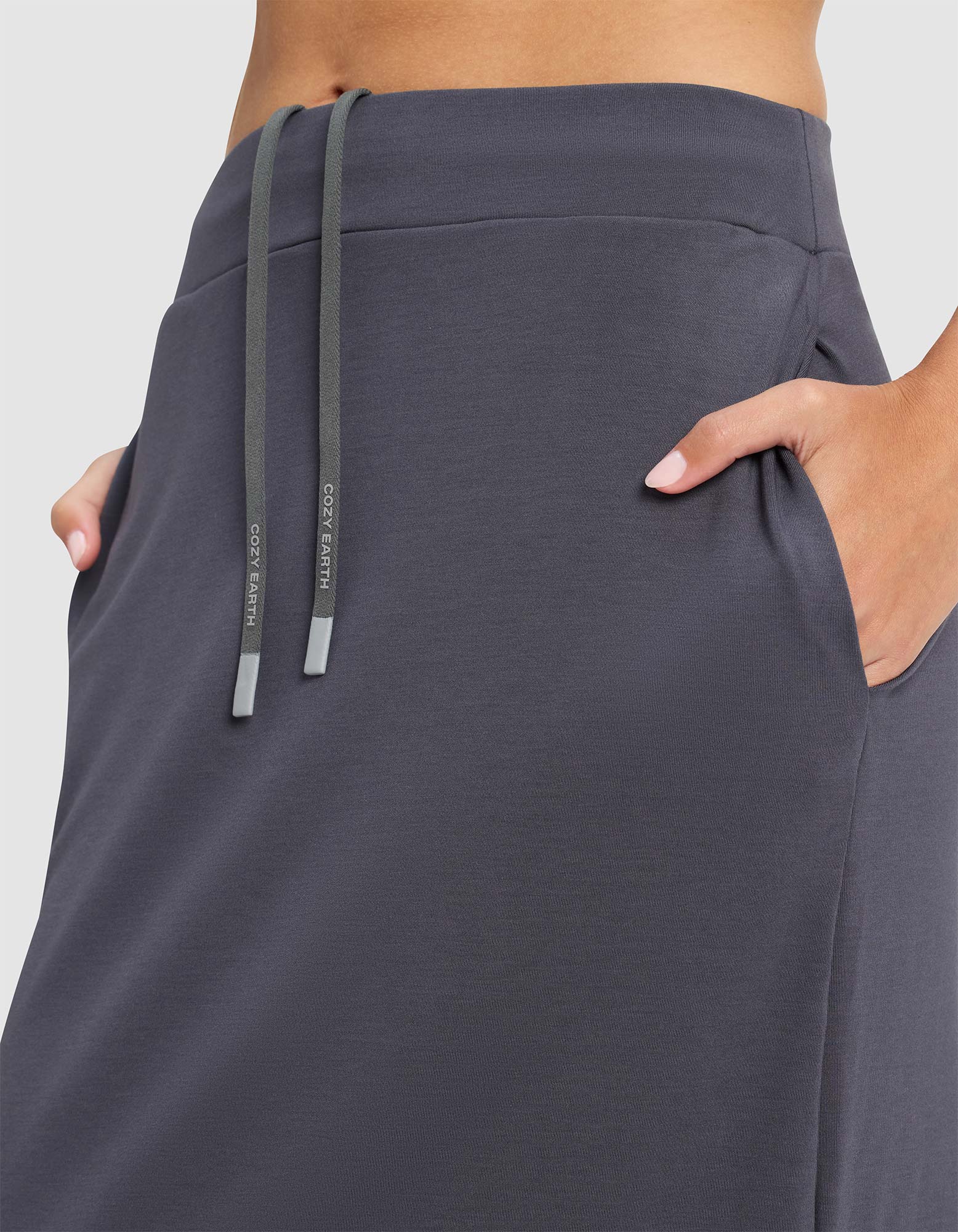 A woman wearing the Cozy Earth Women's Brushed Bamboo Midi Skirt in dark gray, featuring a high waist, side pockets, and a drawstring waistband with two drawstrings hanging down. 