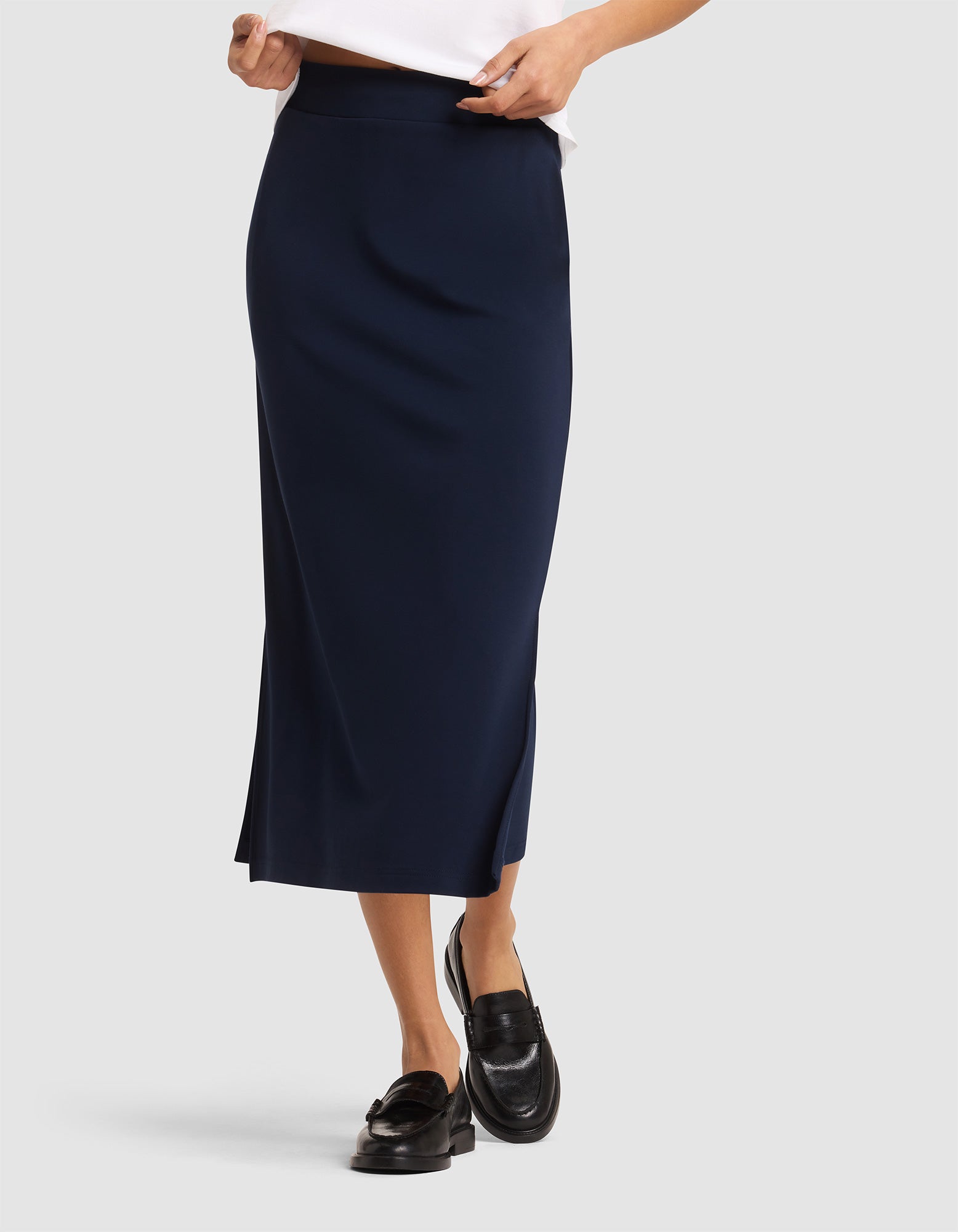 A person wears the Cozy Earth Women's Brushed Bamboo Midi Skirt in navy blue, paired with a white top and black loafers. The photo captures the outfit from the torso down against a plain light background. 