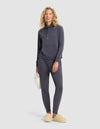 A smiling woman wears the Cozy Earth Women's Brushed Bamboo Mock Neck in dark gray with tan slippers, holding a white water bottle against a plain light background.|Color:Graphite