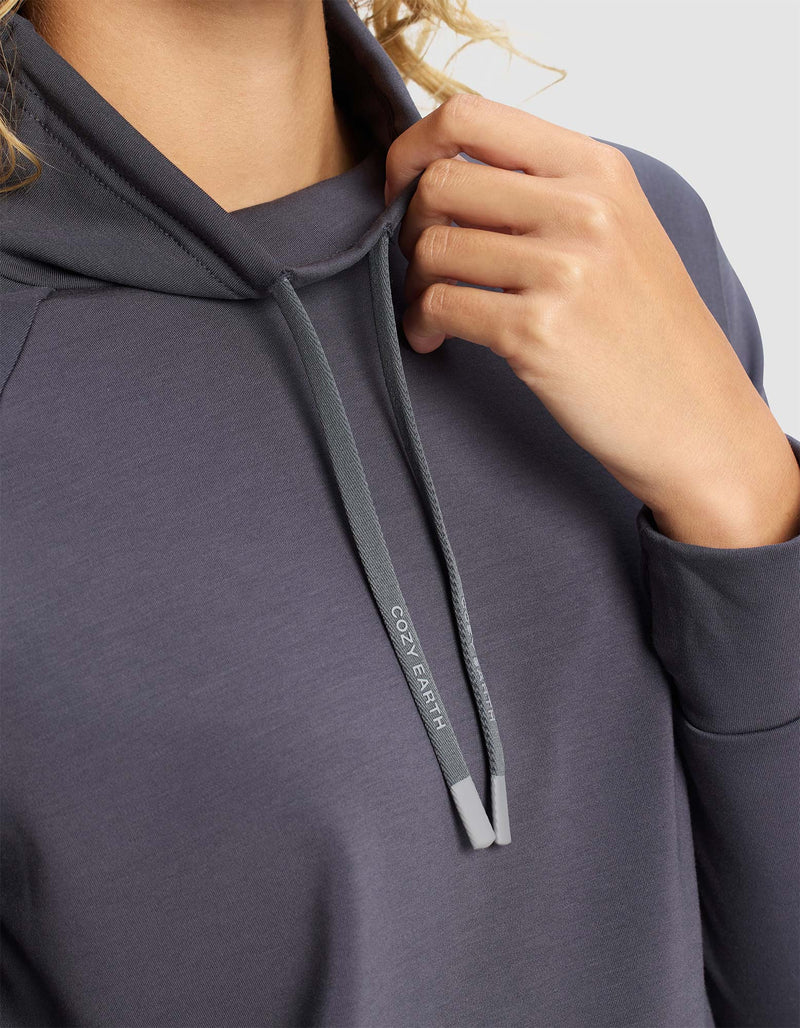 A person wearing the Cozy Earth Women's Brushed Bamboo Mock Neck holds a hood drawstring labeled “COZY EARTH,” with only their hand, part of their arm, neck, and the drawstring visible.