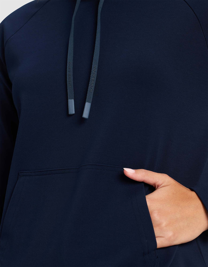 Close-up of a person wearing the Cozy Earth Women's Brushed Bamboo Mock Neck in navy blue, featuring a front pocket, visible drawstrings near the neck, and their right hand partially inside the pocket.