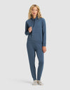 A woman with blonde curly hair wears the Cozy Earth Women's Brushed Bamboo Mock Neck & Jogger Set, paired with striped socks, standing against a plain light background.|Color:Dawn