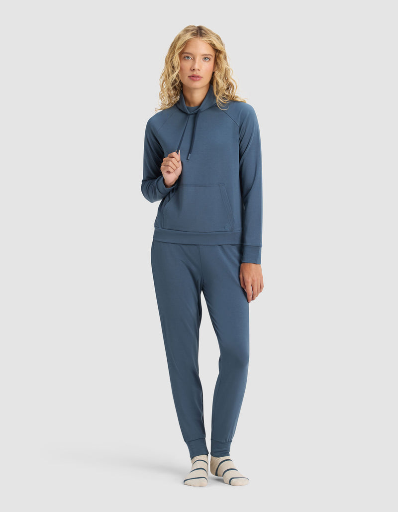 A woman with blonde curly hair wears the Cozy Earth Women's Brushed Bamboo Mock Neck & Jogger Set, paired with striped socks, standing against a plain light background.