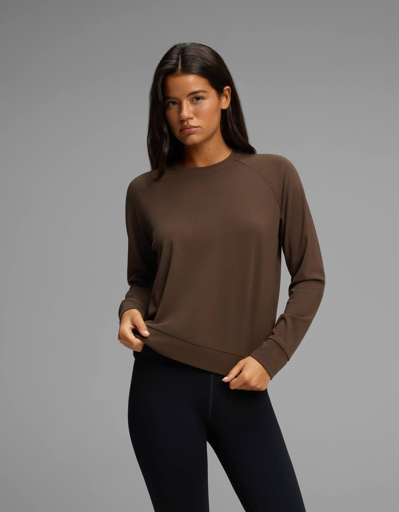 A woman with long dark hair is wearing the Cozy Earth Women's Brushed Bamboo Pullover Crew in brown and black leggings, standing against a plain gray background.
