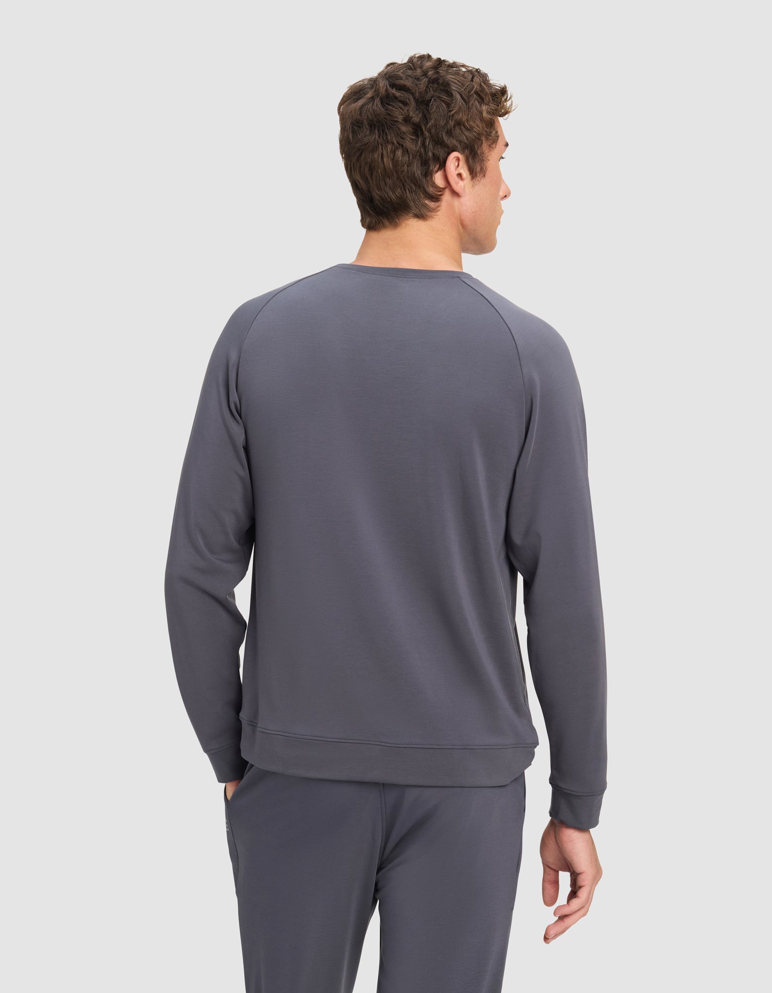 A man faces away, displaying the back of his outfit—Cozy Earth’s Men's Brushed Bamboo Pullover Crew—in gray, set against a plain light gray background.