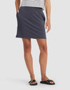 A person stands with hands in pockets, wearing Cozy Earth's Women's Brushed Bamboo Skirt in navy, a white and black striped short-sleeve top, and black slide sandals featuring gold details.