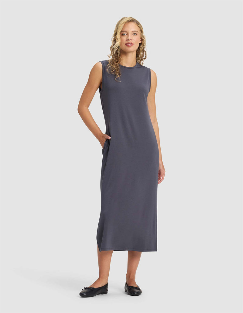 A woman with blonde curly hair wears the Cozy Earth Women's Brushed Bamboo Sleeveless Midi Dress in dark gray with black flats, standing against a plain light background, one hand in her pocket.