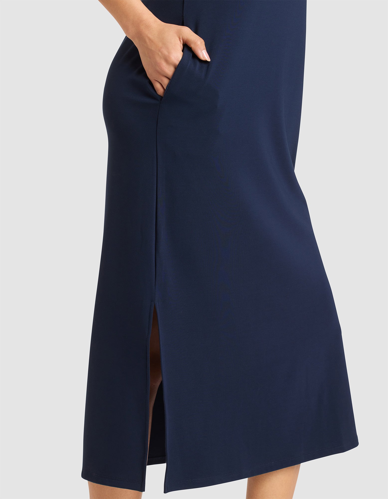 The lower half of a person is shown wearing the Cozy Earth Women's Brushed Bamboo Sleeveless Midi Dress in navy blue, featuring a side pocket and side slit, standing against a light gray background. 
