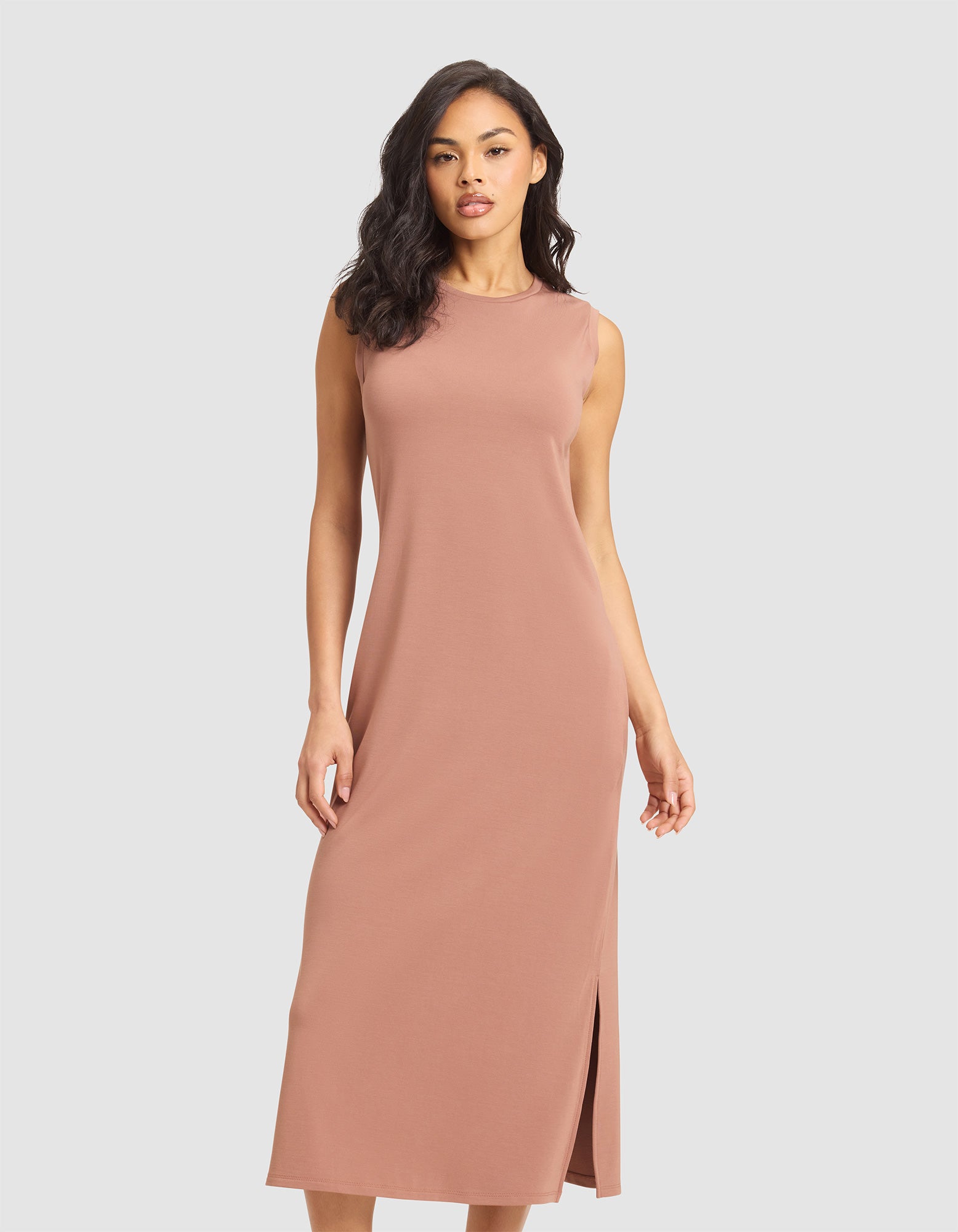 A woman models the Cozy Earth Women's Brushed Bamboo Sleeveless Midi Dress in dusty pink, featuring a side slit, against a plain light gray background. 
