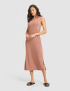 A woman models the Cozy Earth Women's Brushed Bamboo Sleeveless Midi Dress in light brown, paired with black slide sandals featuring gold accents, posing against a plain light gray background. |Color:Saddle