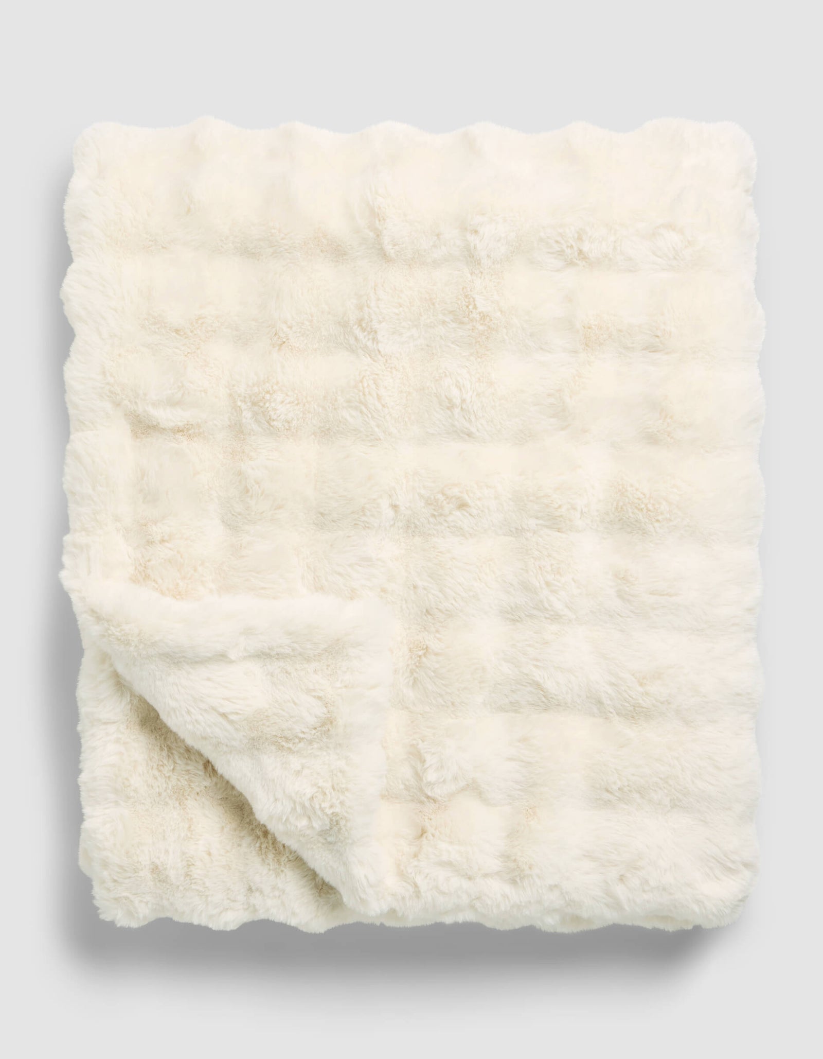 The Cozy Earth Bubble Cuddle Blanket, in a cream hue, is neatly folded with one corner turned over to highlight its soft and plush faux fur texture on both sides.