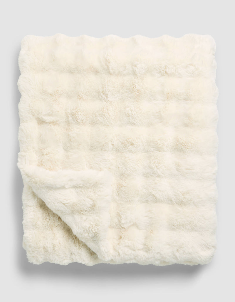 The Cozy Earth Bubble Cuddle Blanket, in a cream hue, is neatly folded with one corner turned over to highlight its soft and plush faux fur texture on both sides.