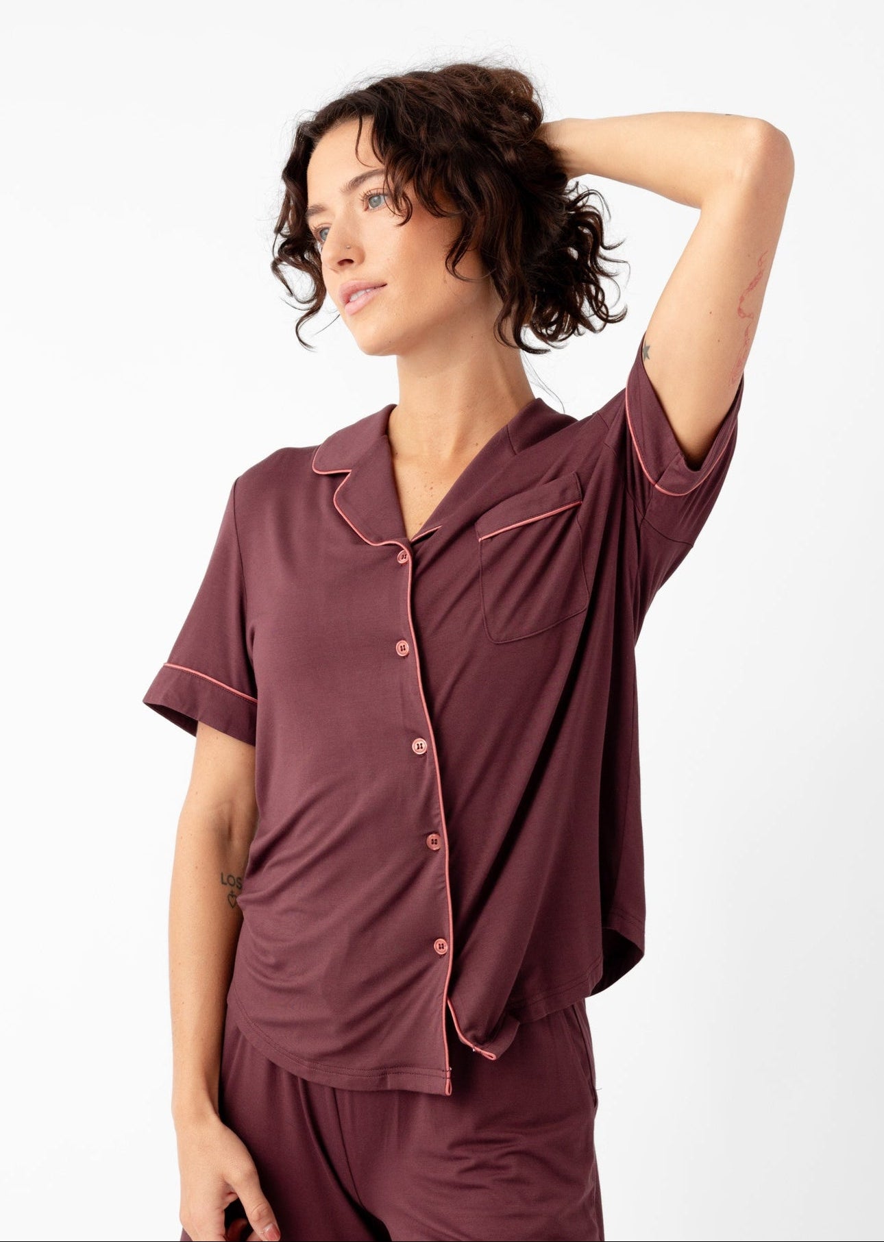 A woman models the Cozy Earth Women's Bamboo Stretch-Knit Short Sleeve Pajama Set, featuring a maroon, button-up top and matching shorts, standing in a relaxed pose against a plain white background.