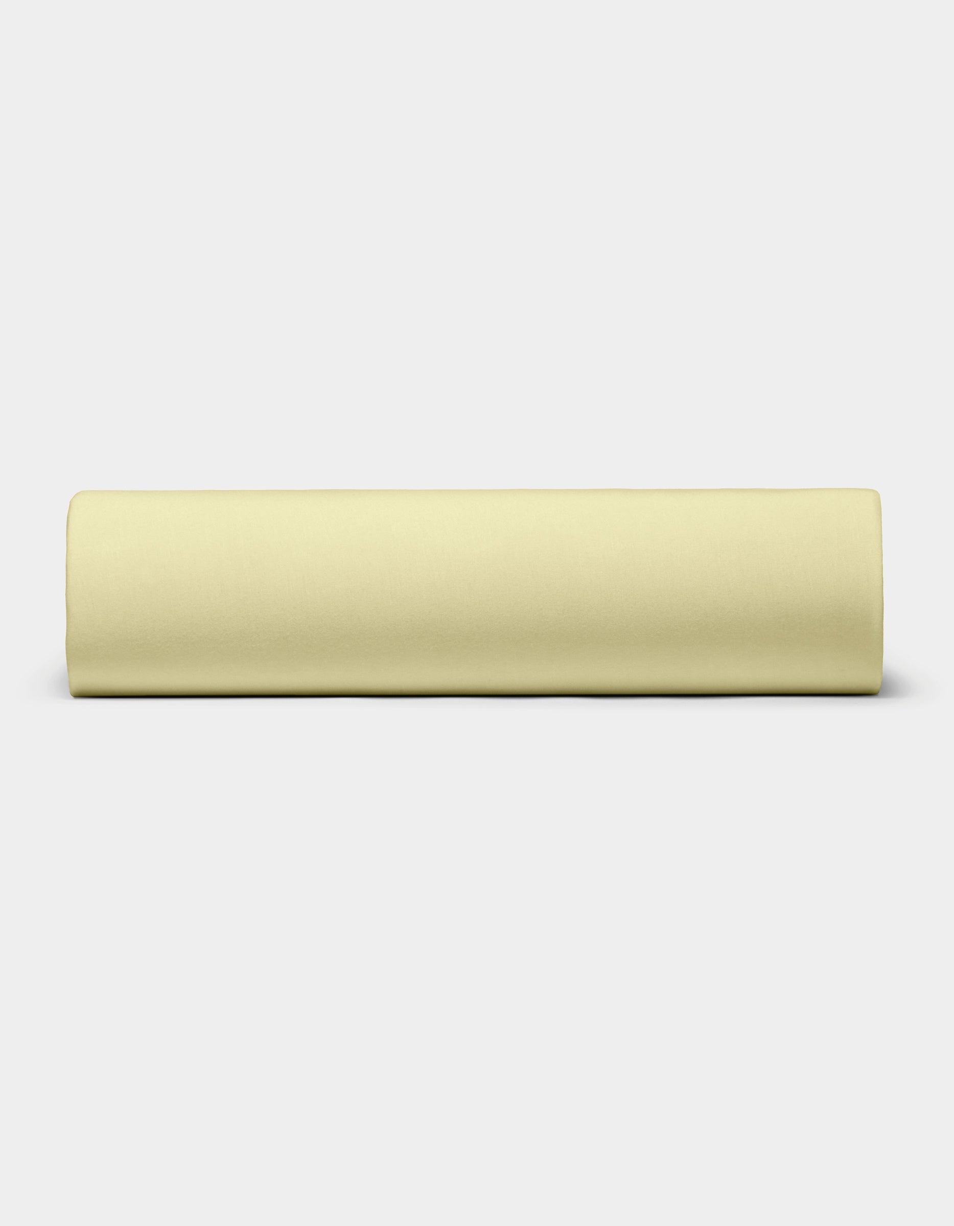 The Bamboo Jersey Sheet Set by Cozy Earth, in pale yellow, is neatly rolled and placed horizontally on a plain white background.|Color:Meringue