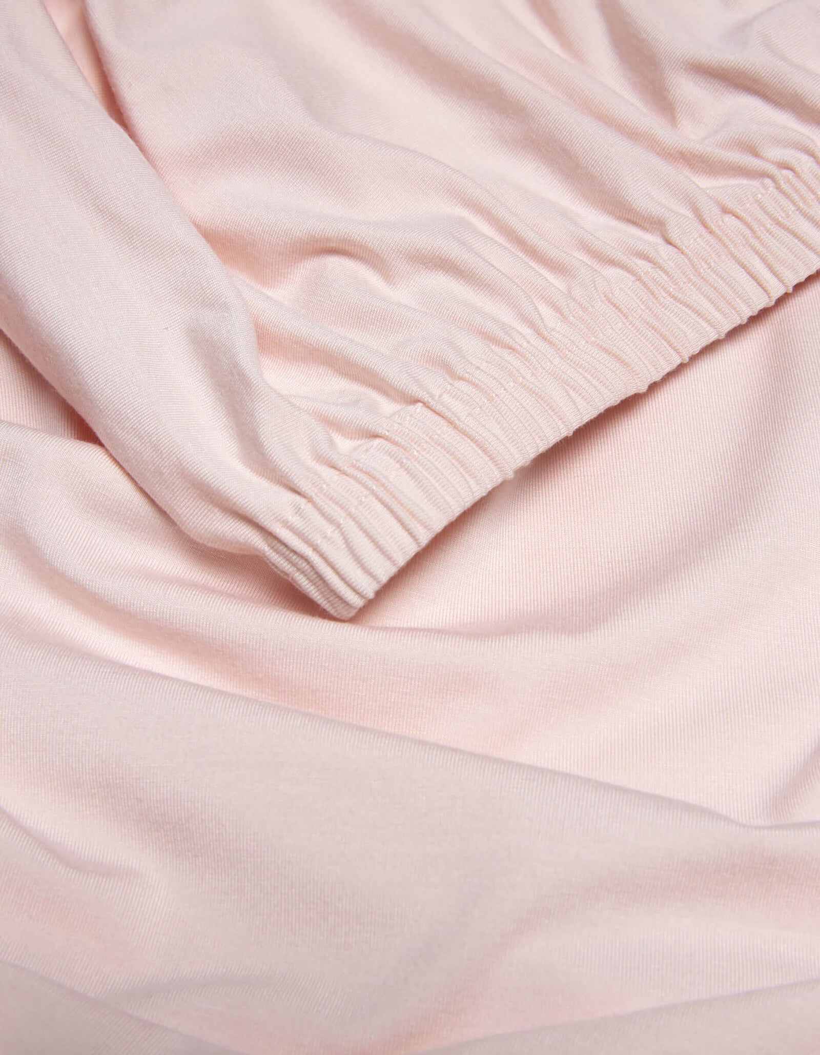 Close-up of Cozy Earth’s Bamboo Jersey Fitted Sheet in light pink, highlighting its smooth texture, soft folds, and gathered elastic cuff detail.