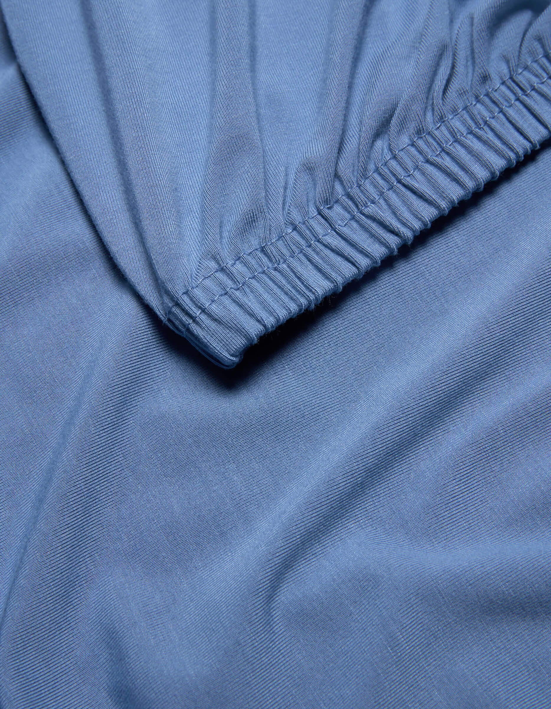 Close-up of light blue Bamboo Jersey Fitted Sheet by Cozy Earth, featuring an elastic edge, smooth texture, and gentle folds.|Color:Sailor