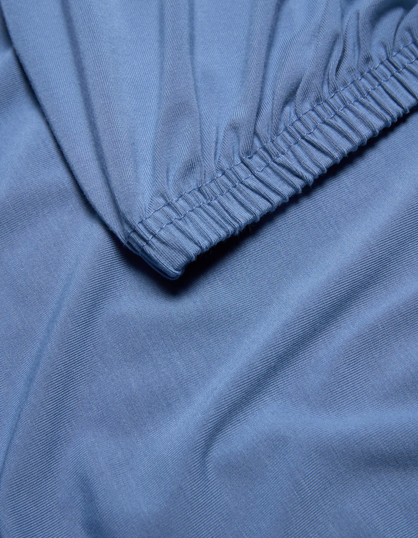 Close-up of light blue Bamboo Jersey Fitted Sheet by Cozy Earth, featuring an elastic edge, smooth texture, and gentle folds.