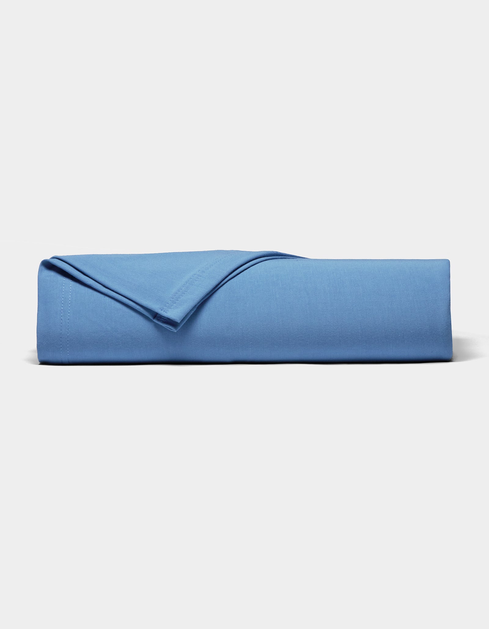 A neatly folded Bamboo Jersey Sheet Set by Cozy Earth in blue rests on a plain white surface, with one corner flipped to display the soft fabric texture.