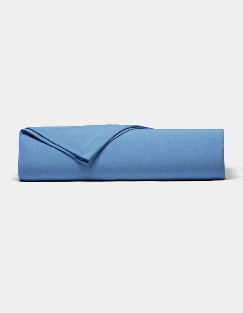 A neatly folded Bamboo Jersey Sheet Set by Cozy Earth in blue rests on a plain white surface, with one corner flipped to display the soft fabric texture.