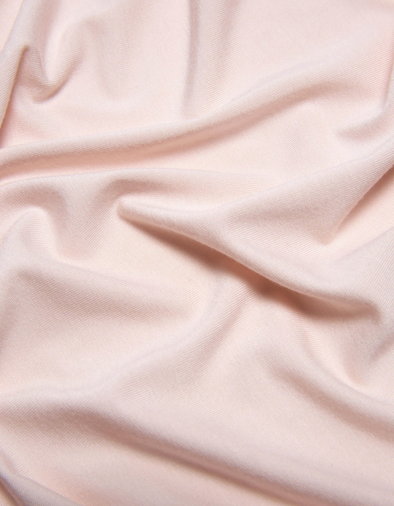 The Bamboo Jersey Sheet Set by Cozy Earth features soft, light pink fabric with subtle folds and gentle wrinkles for a smooth, slightly textured look.