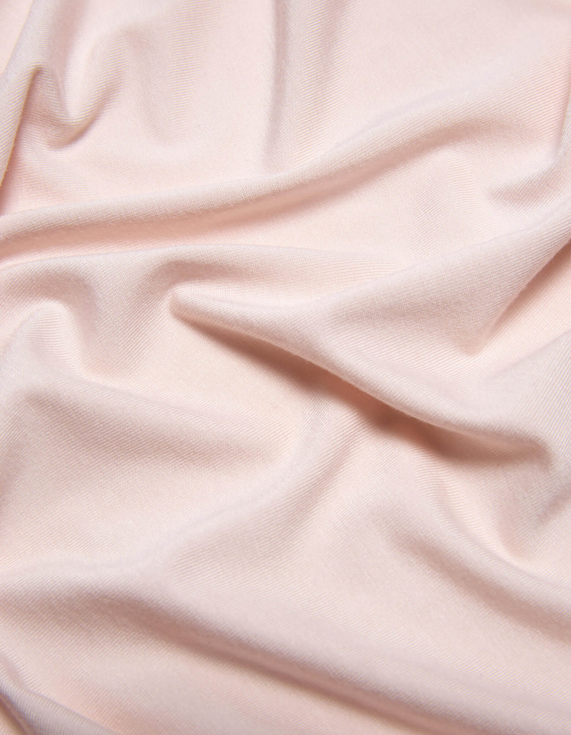 The Bamboo Jersey Sheet Set by Cozy Earth features soft, light pink fabric with subtle folds and gentle wrinkles for a smooth, slightly textured look.|Color:Petal