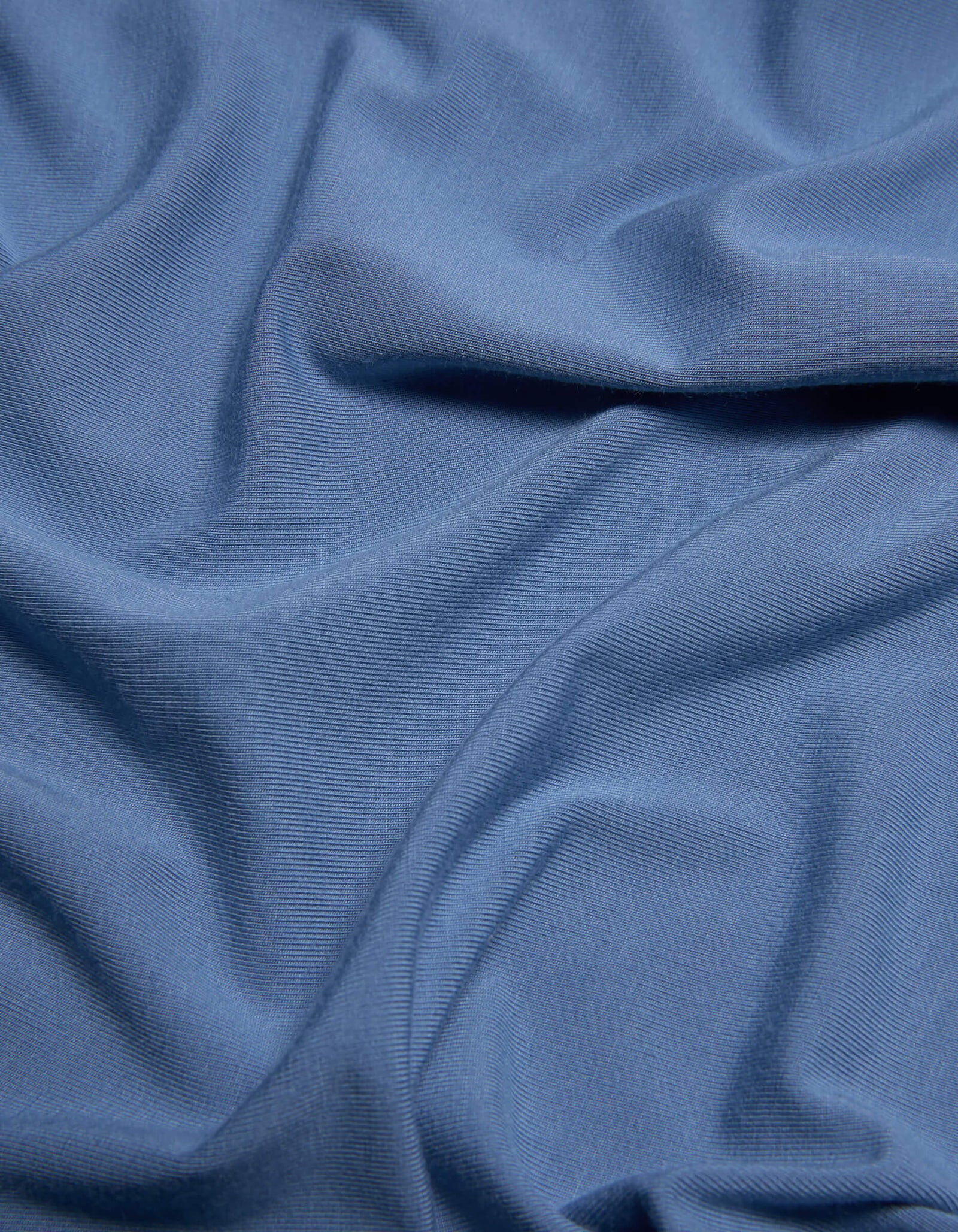 A close-up of Cozy Earth’s Bamboo Jersey Sheet Set in light blue, highlighting the gentle folds, soft creases, and subtle textured pattern on its surface.