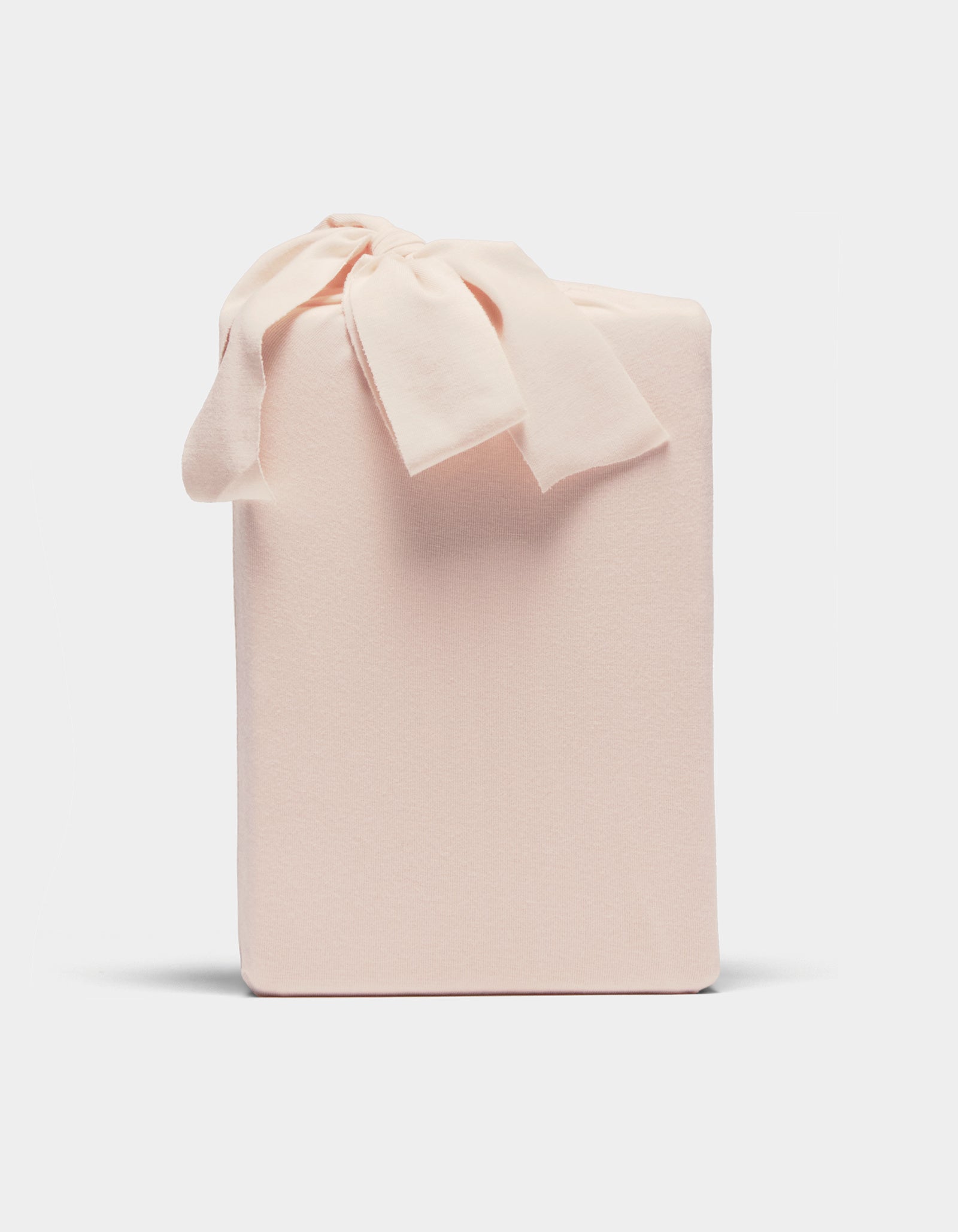 A Bamboo Jersey Sheet Set by Cozy Earth, neatly wrapped in pale pink fabric with a matching bow on top, displayed against a plain white background.