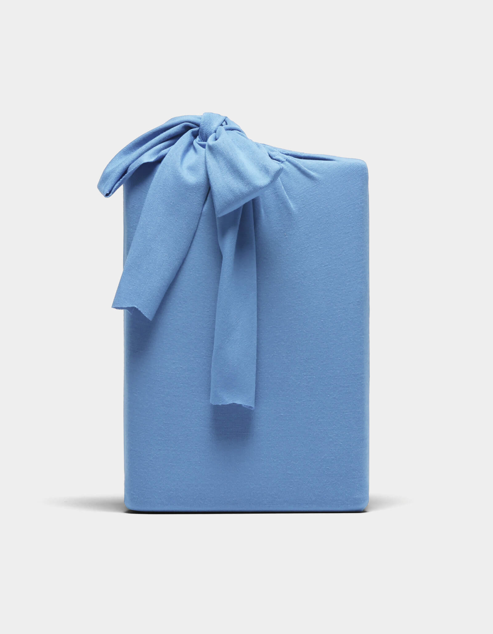 A Bamboo Jersey Sheet Set by Cozy Earth, neatly folded and wrapped in light blue fabric with a matching bow, displayed against a plain white background.