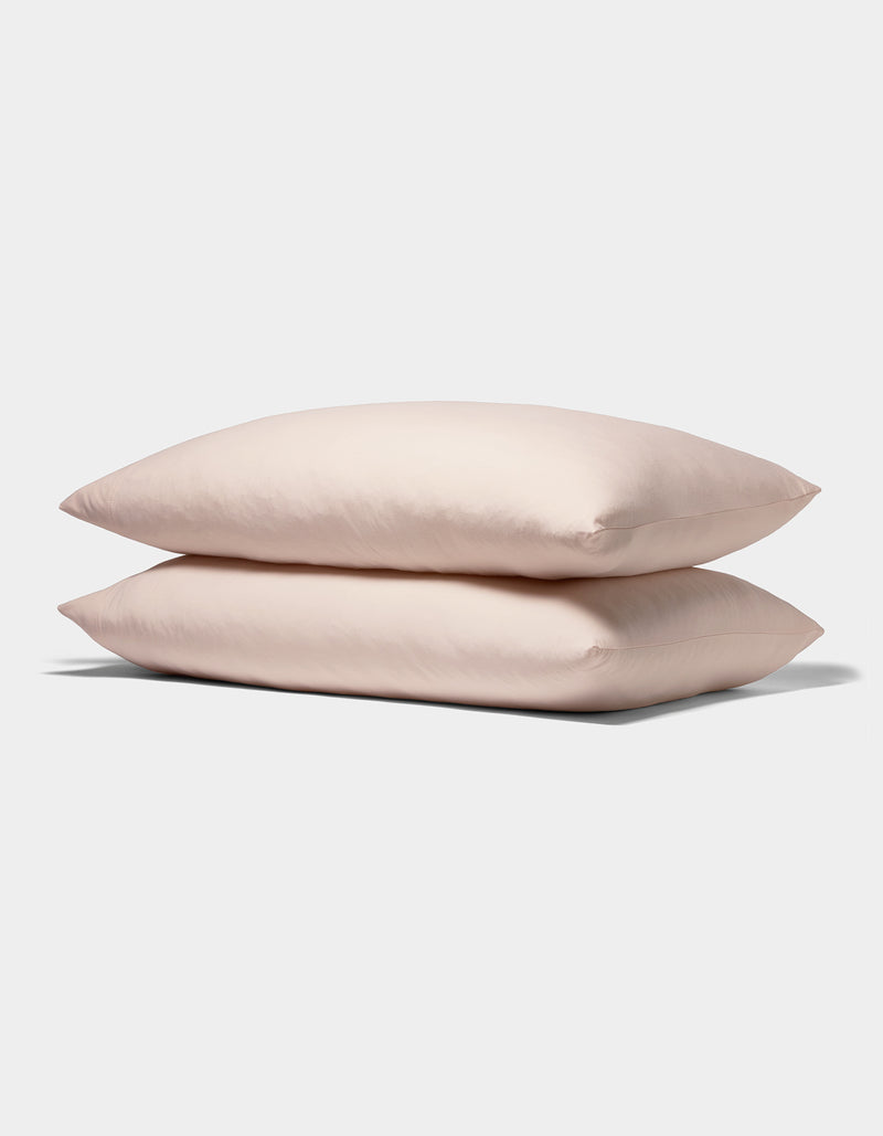 Two Bamboo Jersey Pillowcases from Cozy Earth, in soft light pink, are stacked neatly against a plain white background.