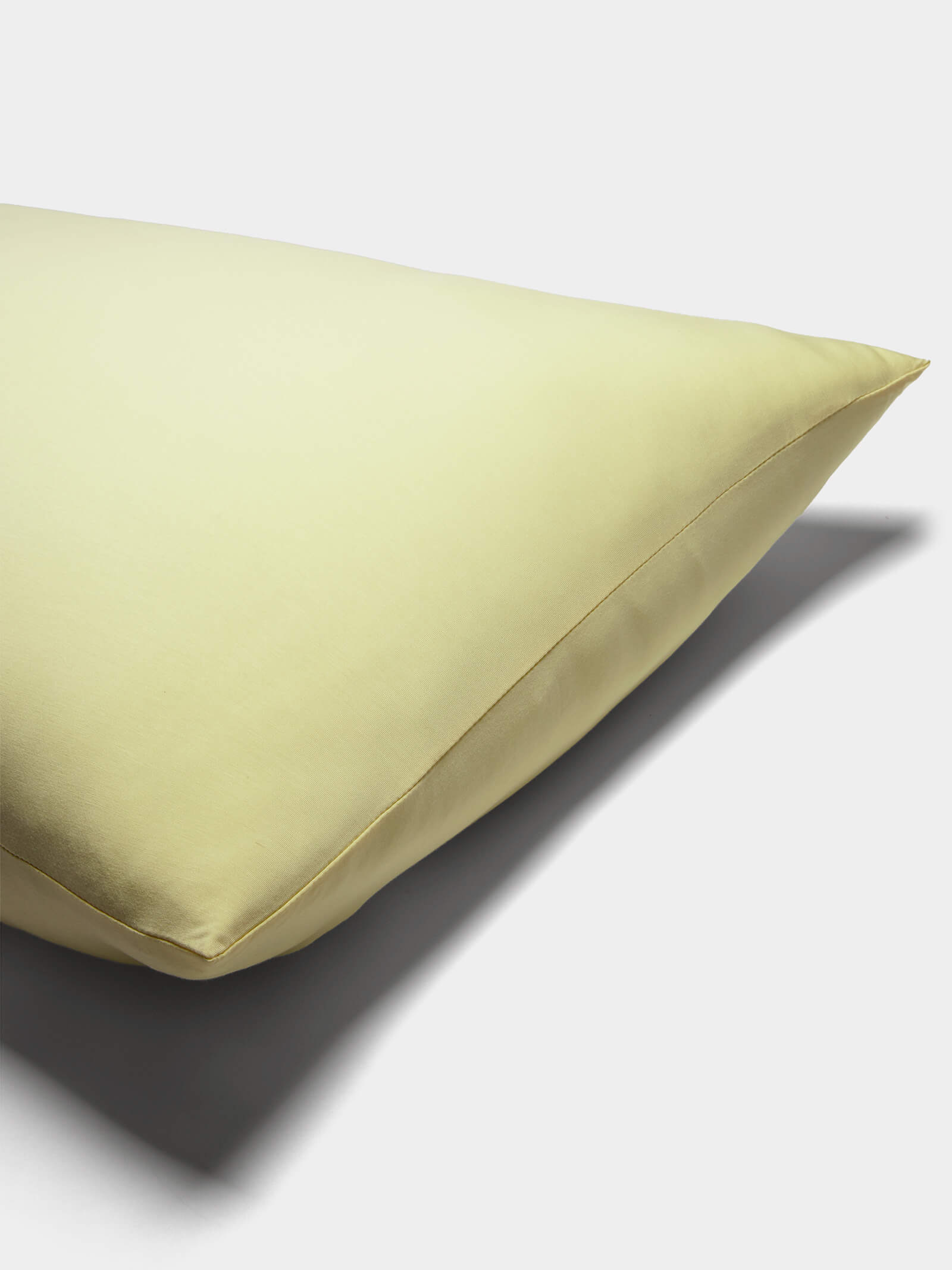 A close-up of a pale yellow Cozy Earth Bamboo Jersey Pillowcase with a smooth surface, set on a white background and casting a soft shadow to the right.