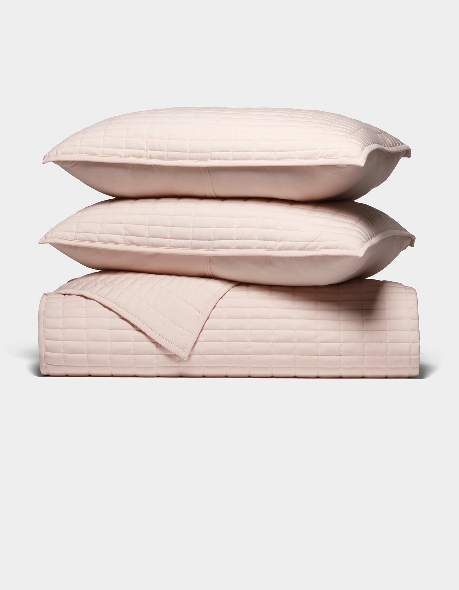 The Cozy Earth Bamboo Jersey Quilt Bundle features two light pink quilted pillows stacked atop a matching quilted blanket, all neatly arranged against a plain white background.