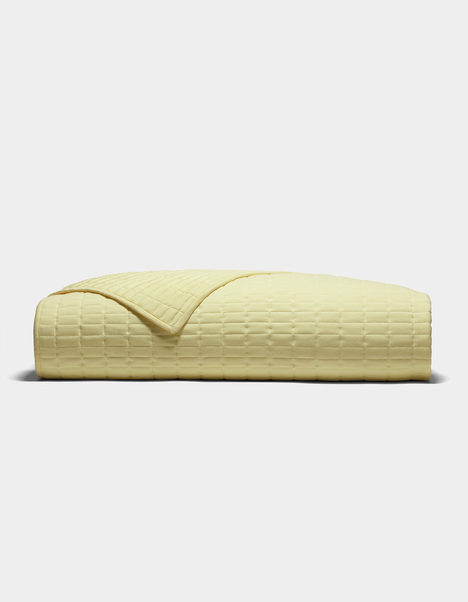 The Cozy Earth Bamboo Jersey Quilt, shown folded from the side on a plain light background, features a pale yellow color and a subtle grid-like textured pattern.