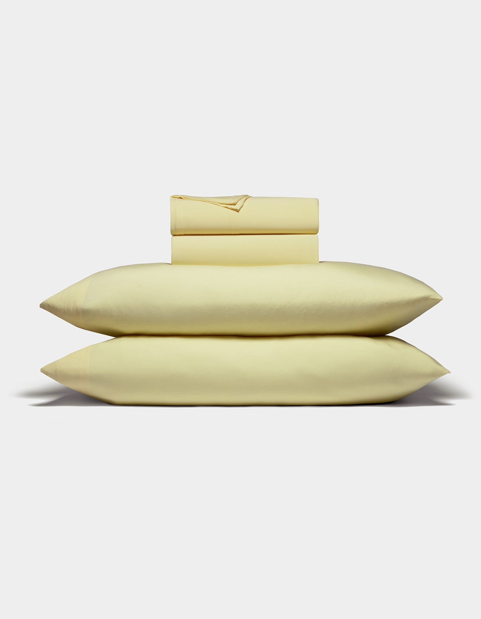 The Cozy Earth Bamboo Jersey Sheet Set is displayed neatly folded with two stacked pillows, a flat sheet, and a fitted sheet in light yellow against a plain white background.