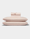 A neatly folded stack of Cozy Earth's Bamboo Jersey Sheet Set, in pale pink, featuring two pillows, a fitted sheet, a flat sheet, and pillowcases arranged on a white background.|Color:Petal