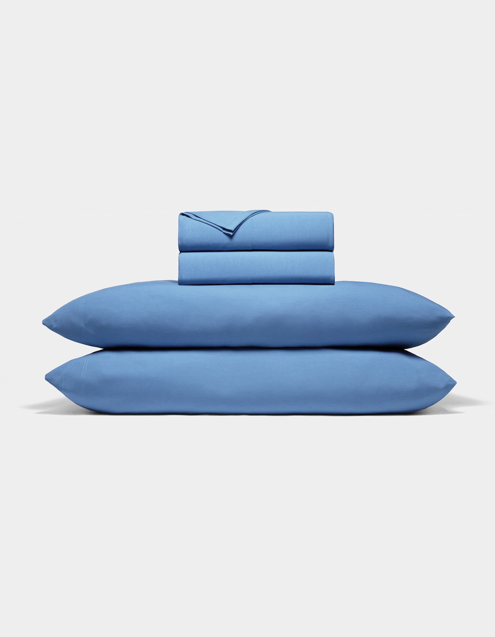 The Cozy Earth Bamboo Jersey Sheet Set, featuring two pillowcases, a fitted sheet, and a flat sheet in blue, is neatly folded and stacked against a plain white background.