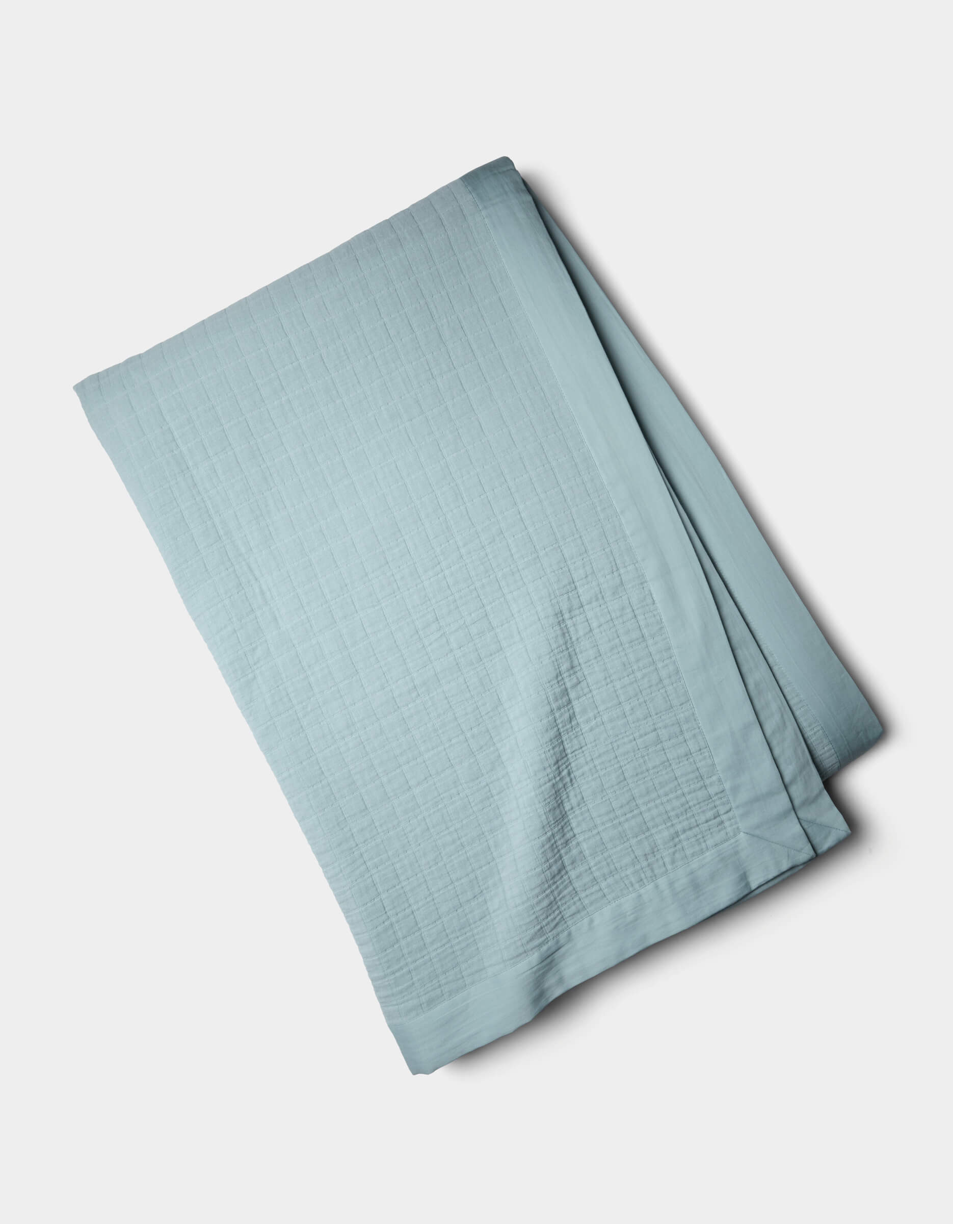 The Cozy Earth Waterfront Grid Matelasse Blanket, in light blue with a subtle grid pattern, is neatly folded and displayed on a plain white background.