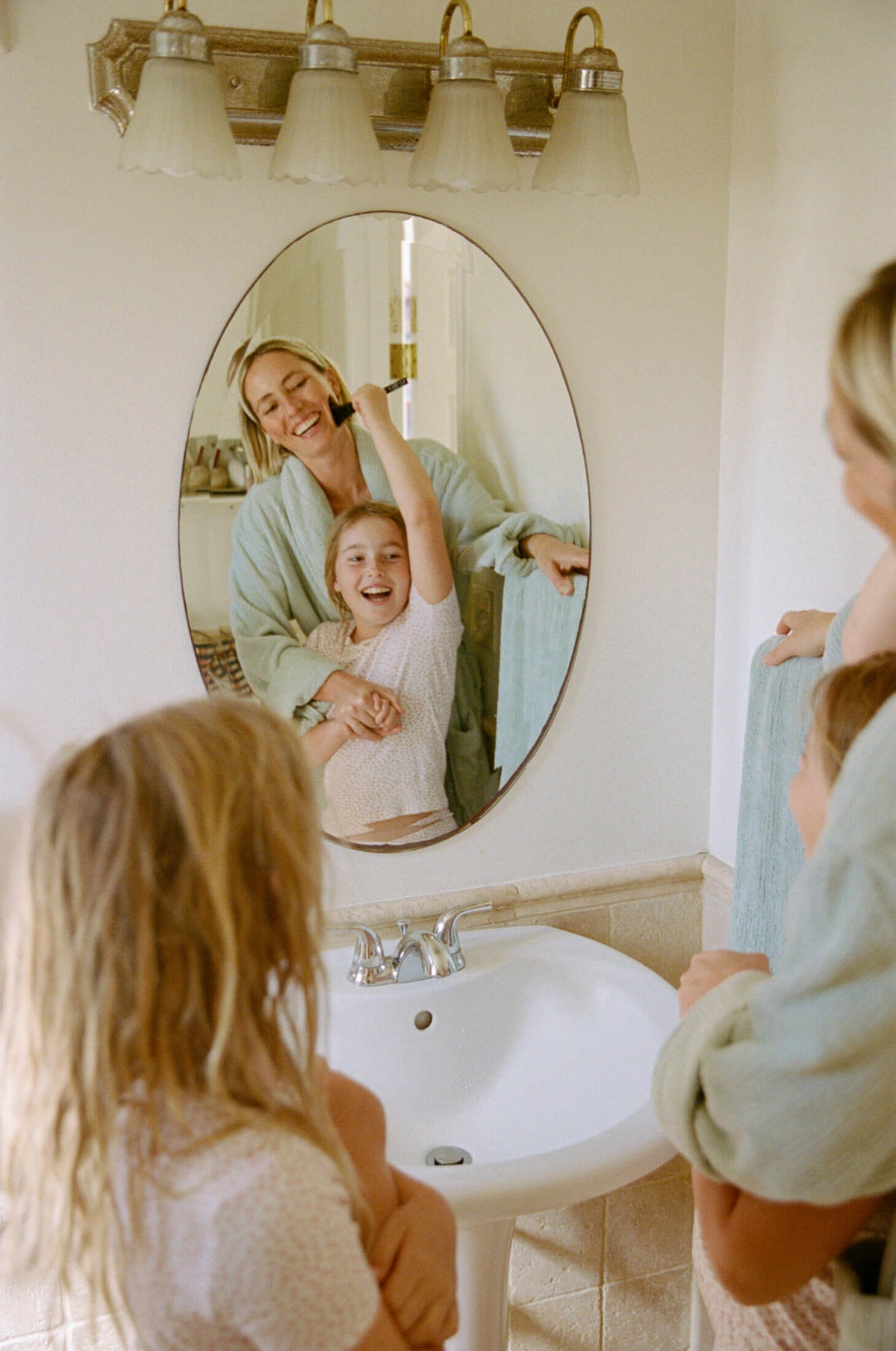 Woman and two children in a bathroom with a mirror reflecting their actions.
