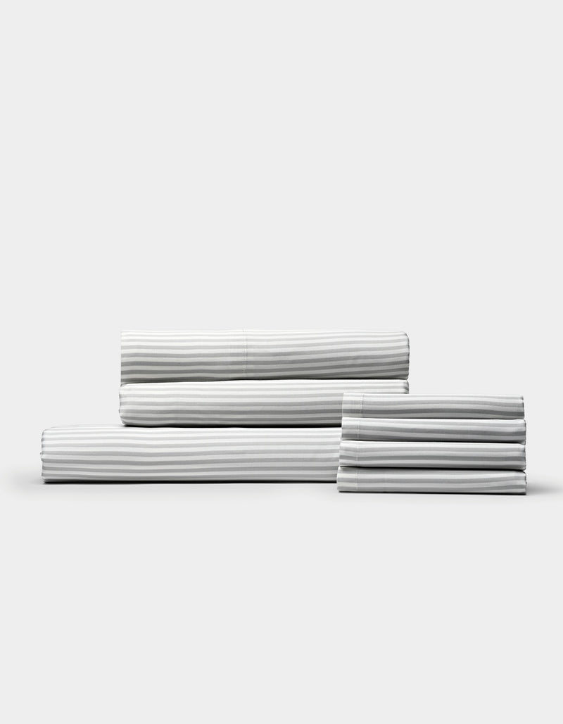 A neatly stacked set of Cozy Earth Bamboo Bedding Core Bundle sheets, featuring white fabric with thin grey stripes, displayed against a plain light background.