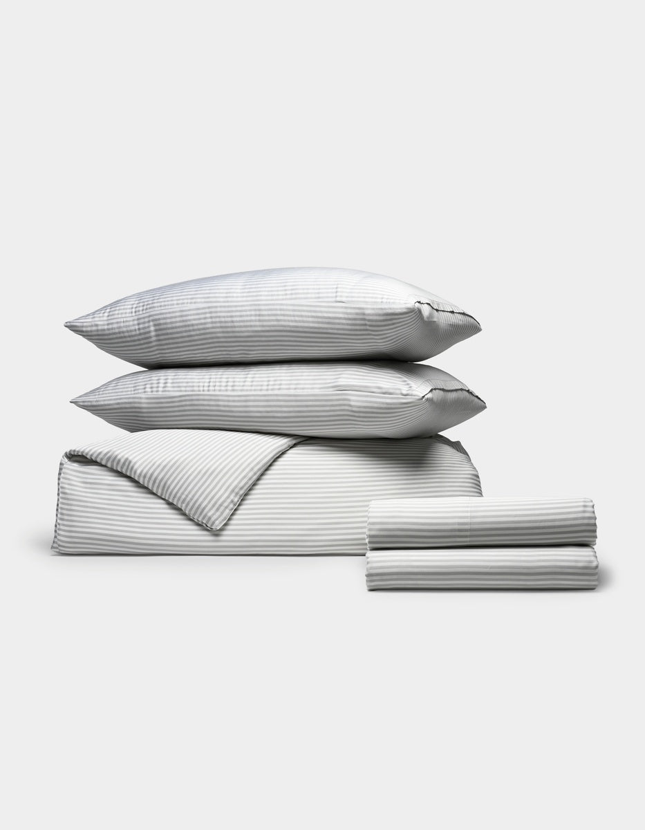 The Cozy Earth Bamboo Bedding Deluxe Bundle, in grey stripes, includes two pillows, a duvet, and sheets neatly folded and displayed on a plain white background.