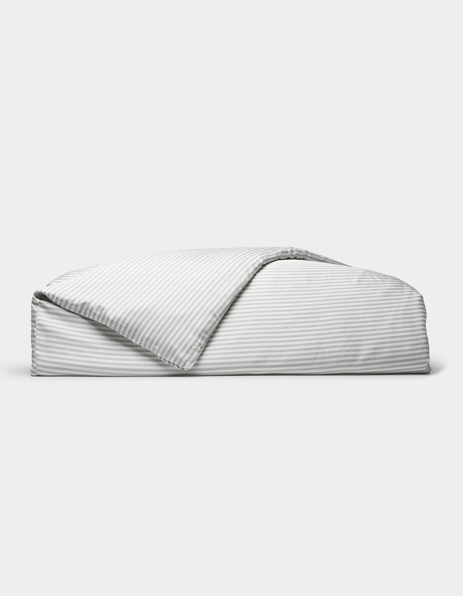 A neatly folded Bamboo Duvet Cover by Cozy Earth, featuring light gray and white stripes with one corner flipped open, is displayed against a plain white background.