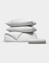 The Cozy Earth Bamboo Bedding Essential Bundle, featuring two stacked pillows, a folded comforter, and a folded sheet in light gray and white thin stripes, is arranged neatly against a plain white background.|Color:Classic Stripe in Dew