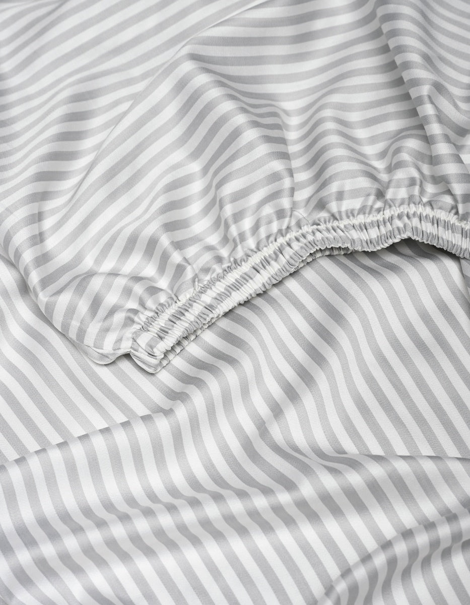 A close-up of the Cozy Earth Bamboo Fitted Sheet displays its gray and white diagonal stripes, featuring a gathered elastic edge and smooth, slightly wrinkled fabric.